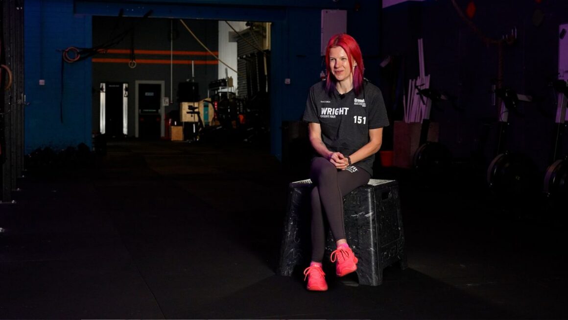 Holly sits on a box in a gym for a case study interview.