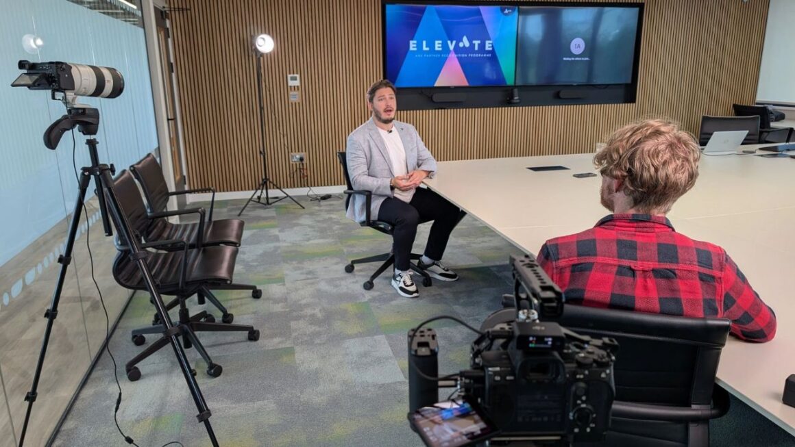 A man being interviewed under lights in a boardroom.
